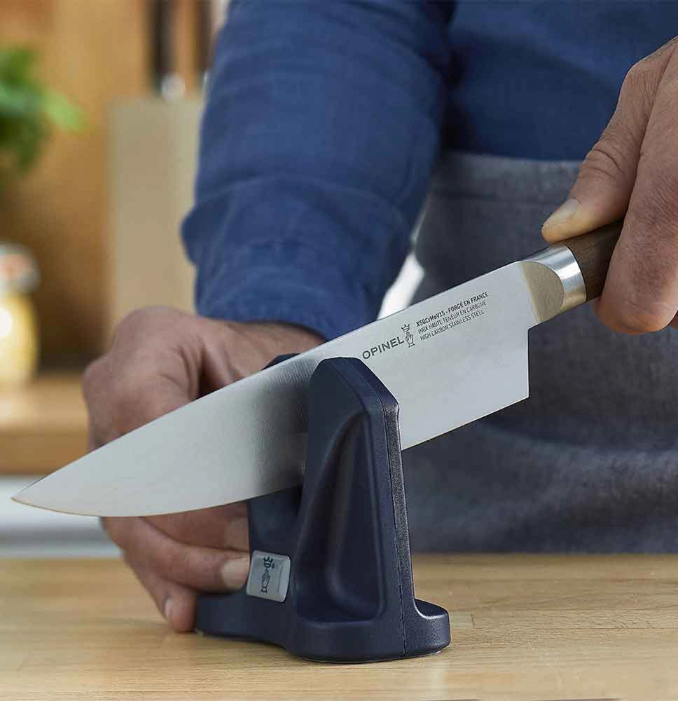 Personne qui aiguise une grande lame de couteau de cuisine Opinel avec l'aiguiseur de la marque