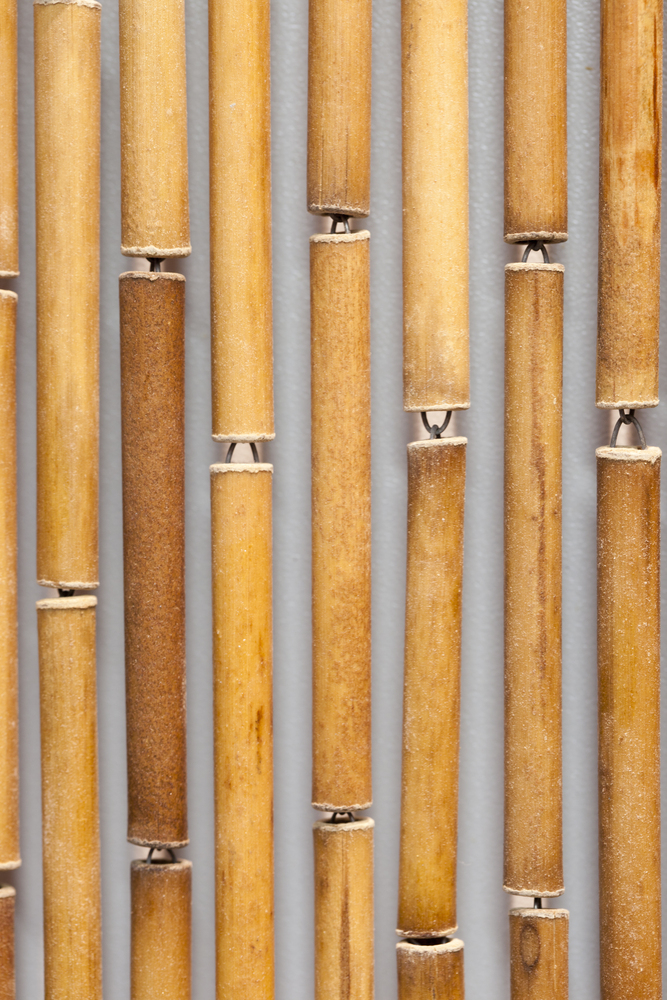 Gros plan sur un rideau de porte composé de tubes en bambou naturel reliés par des crochets métalliques.