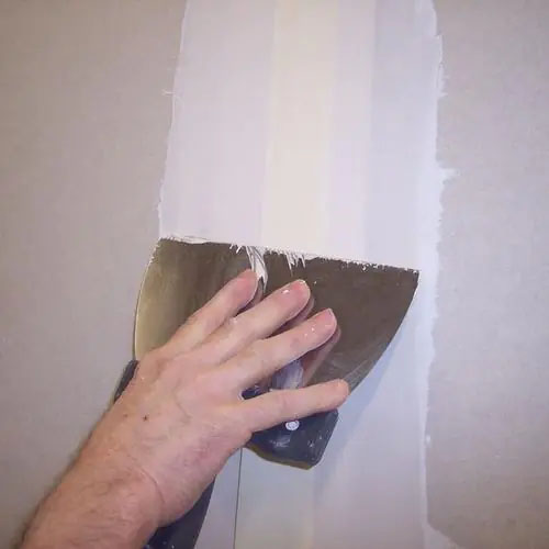 Main qui pose une bande à joint au couteau à enduire sur une plaque de plâtre avec l'enduit en pâte Touprêt