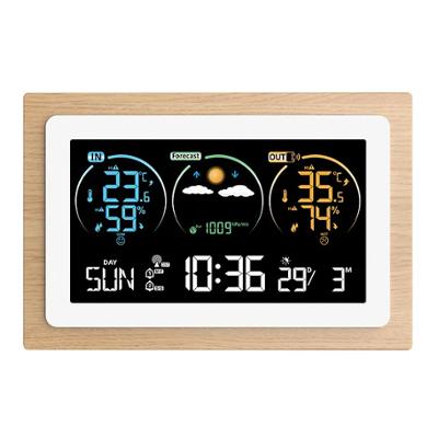 Station météo numérique avec cadre effet bois affichant l'heure, la date, la pression atmosphérique, ainsi que les températures et taux d'humidité intérieurs et extérieurs sur un écran couleur.