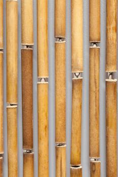 Gros plan sur un rideau de porte composé de tubes en bambou naturel reliés par des crochets métalliques.