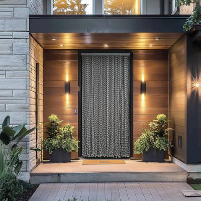 Rideau de porte décoratif en cordes tressées bicolores grises et blanches installé dans une entrée de maison moderne, entouré d'appliques murales lumineuses, de plantes en pots et d'un paillasson au sol.